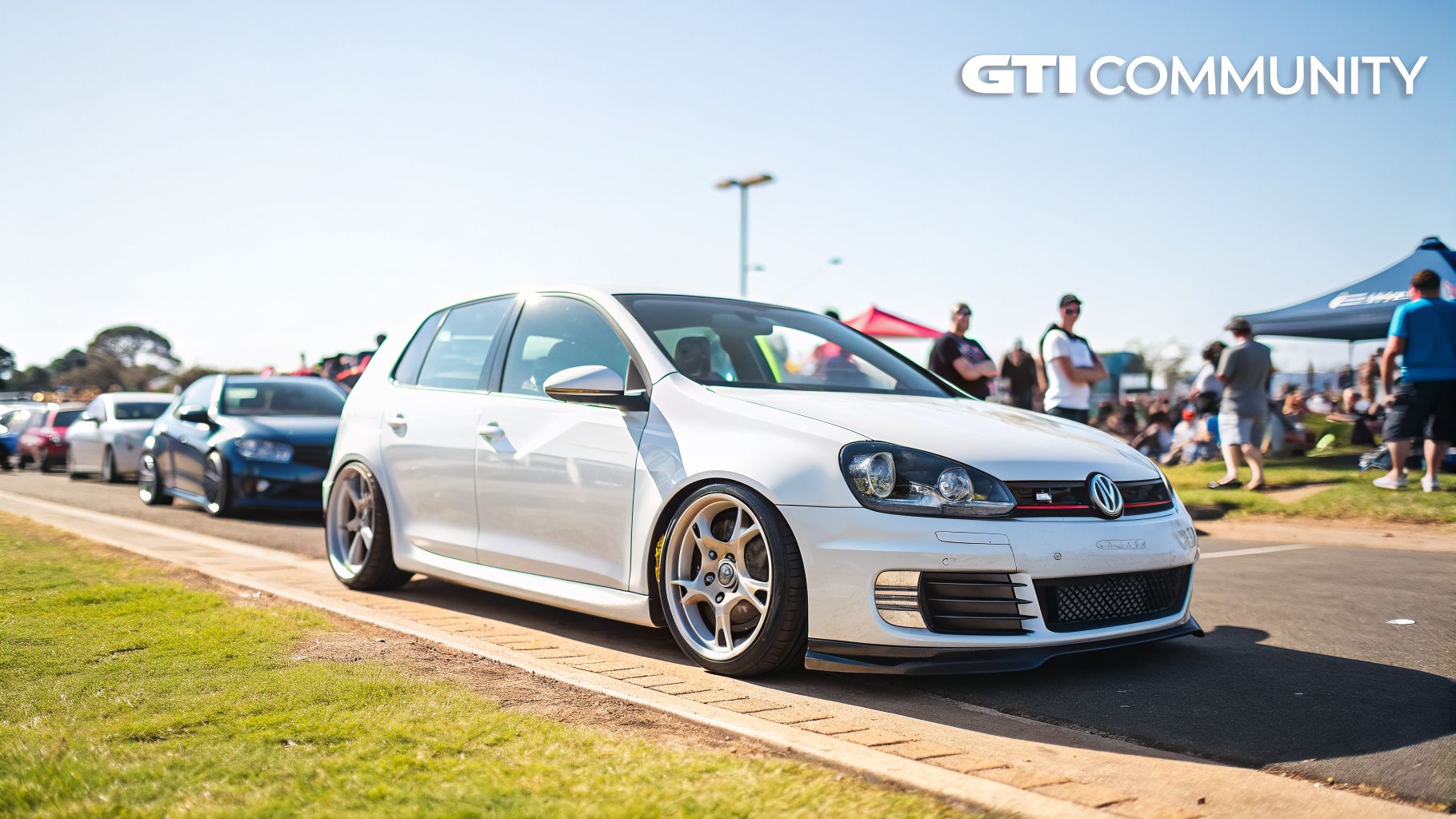 White Volkswagen Golf GTI MK6 lowered on custom wheels at an outdoor car meet.
