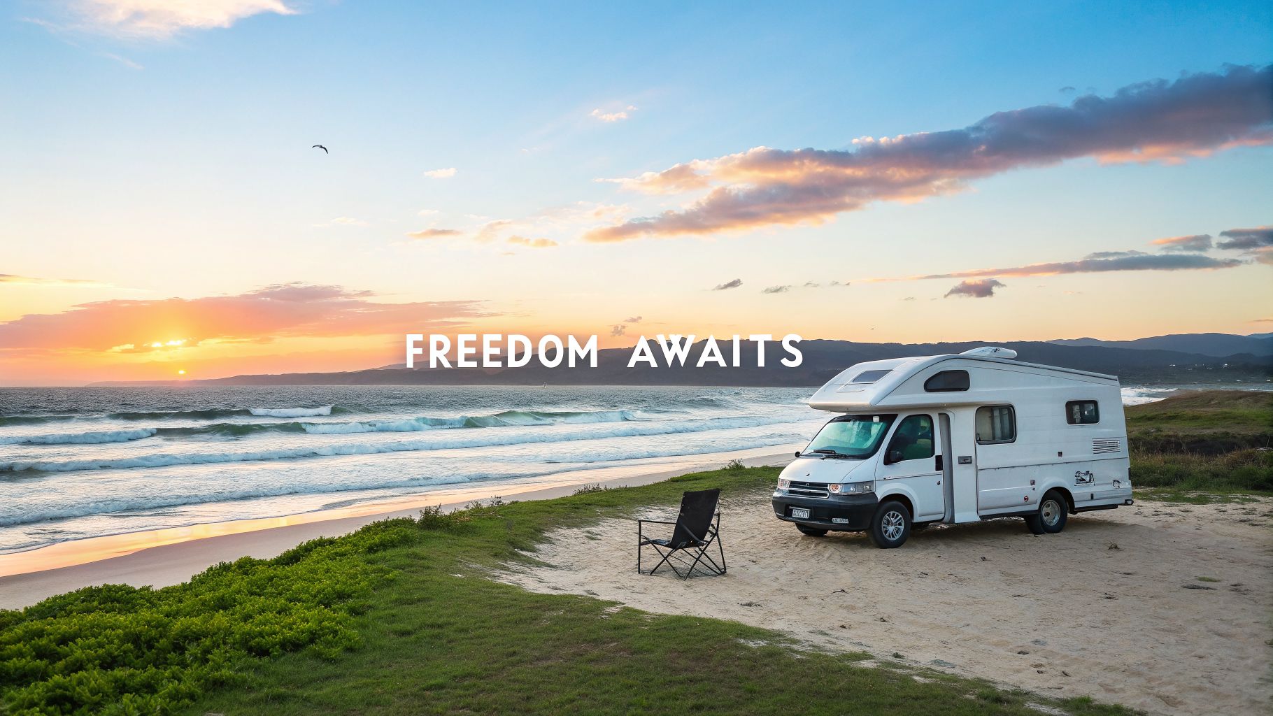 A white campervan with a chair parked on a sandy beach at sunset, overlooking the ocean waves.