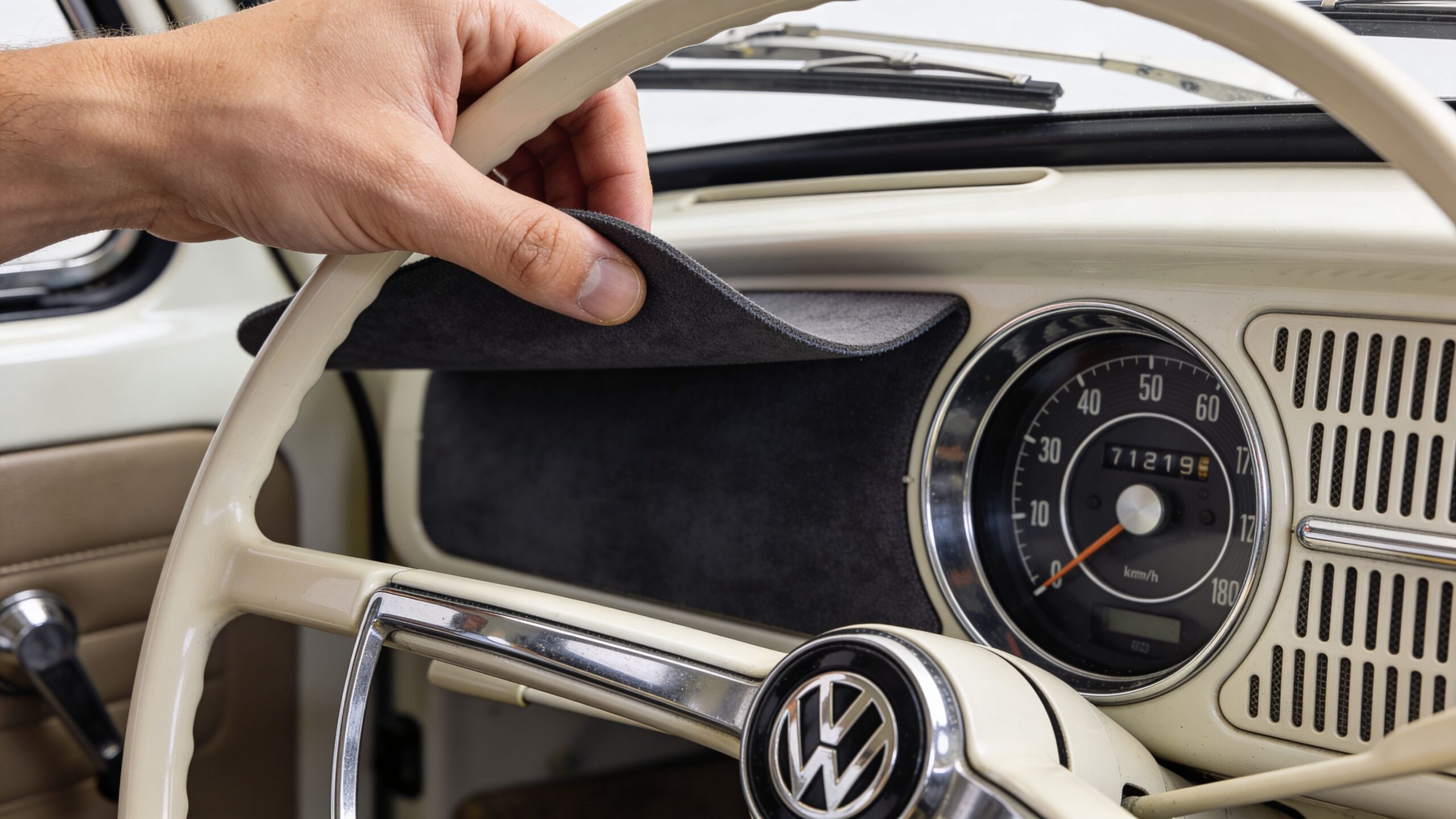 A hand placing a custom gray automotive dashboard cover onto the vintage dashboard of a classic Volkswagen vehicle.