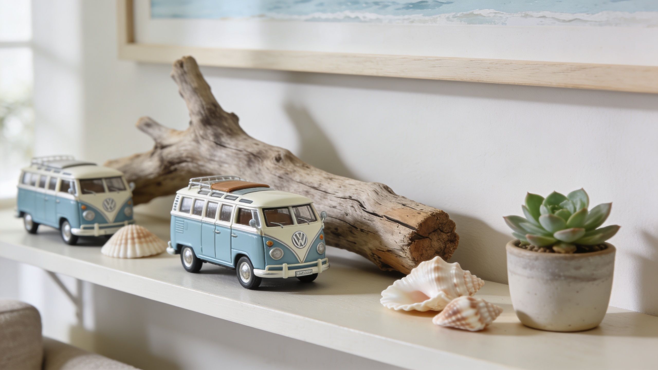Two miniature vintage blue and white Volkswagen bus models displayed on a shelf with seashells and a succulent.