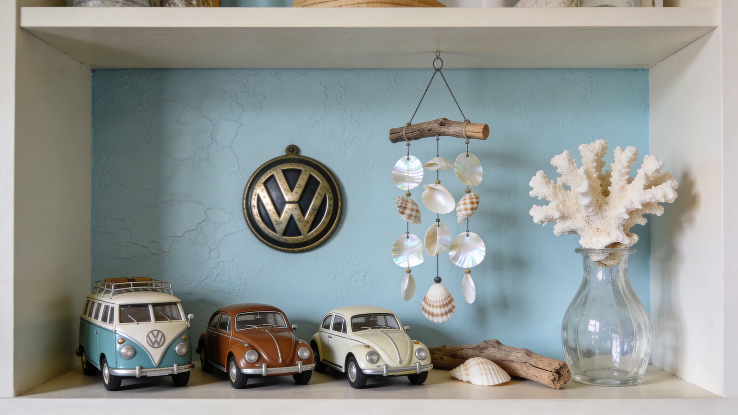 A shelf decorated with Volkswagen model cars, a shell wind chime, and a white piece of coral.