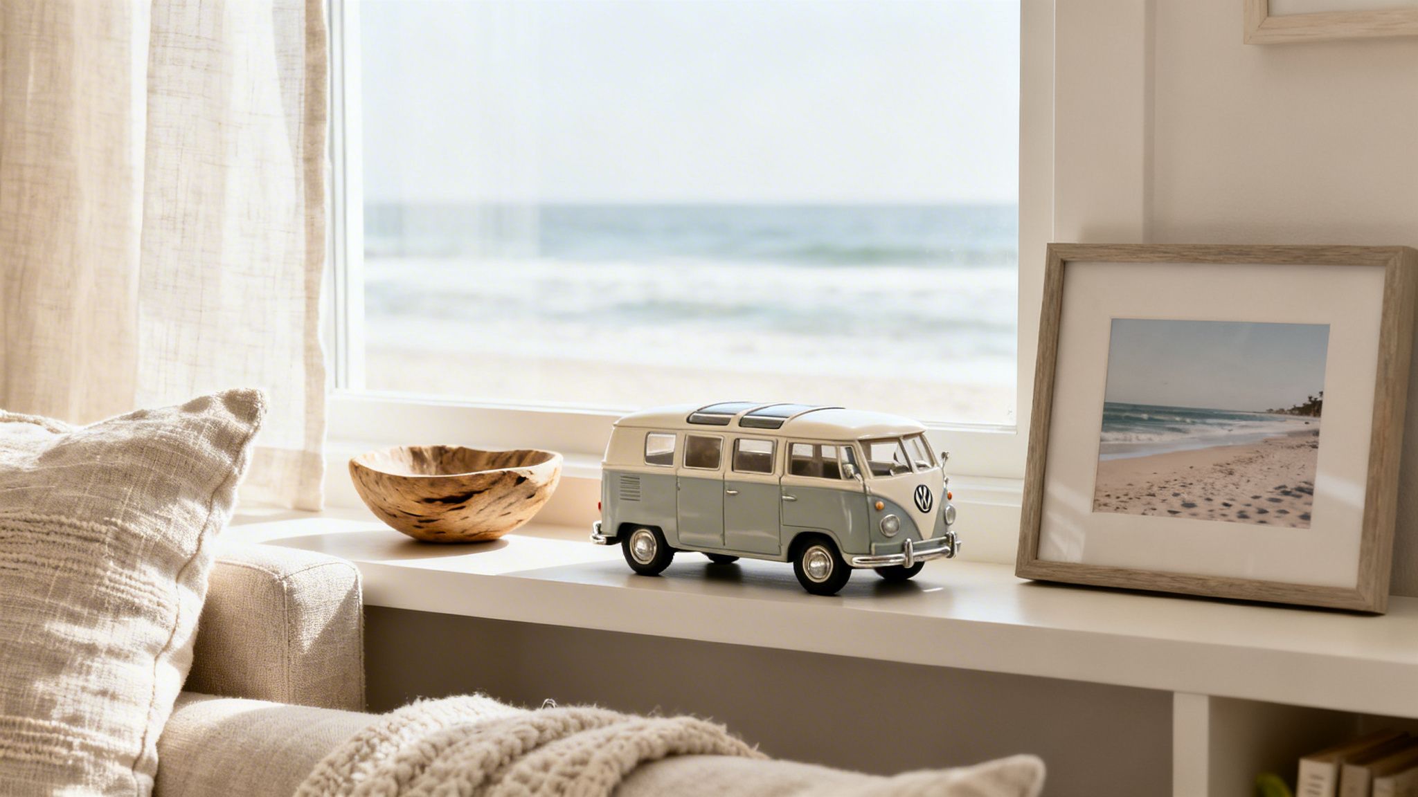 A toy Volkswagen camper van sits on a bright windowsill overlooking a sunny beach.