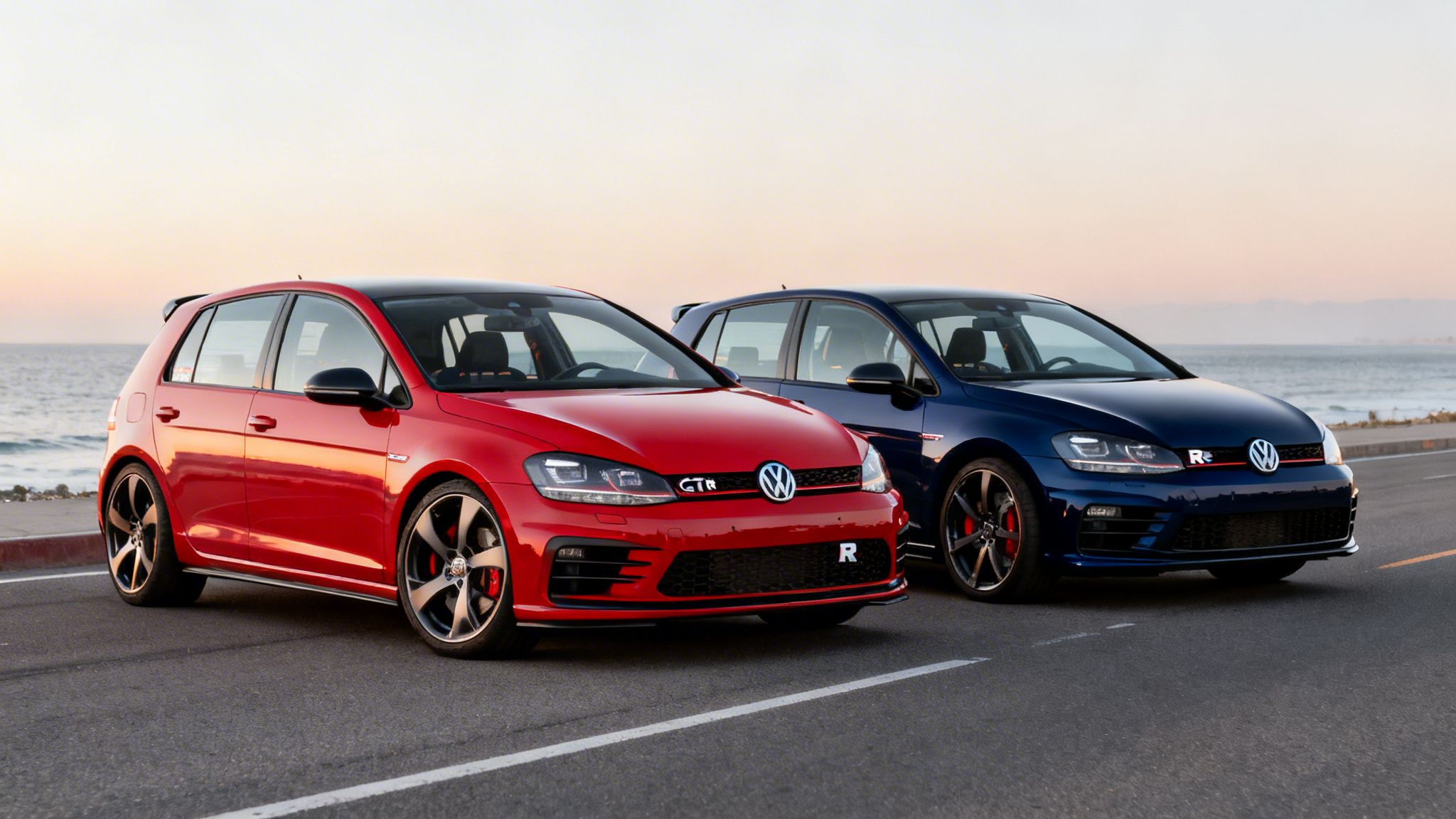 Two Volkswagen Golf MK7 cars, a red GTI and a blue R, parked by the ocean at sunset.