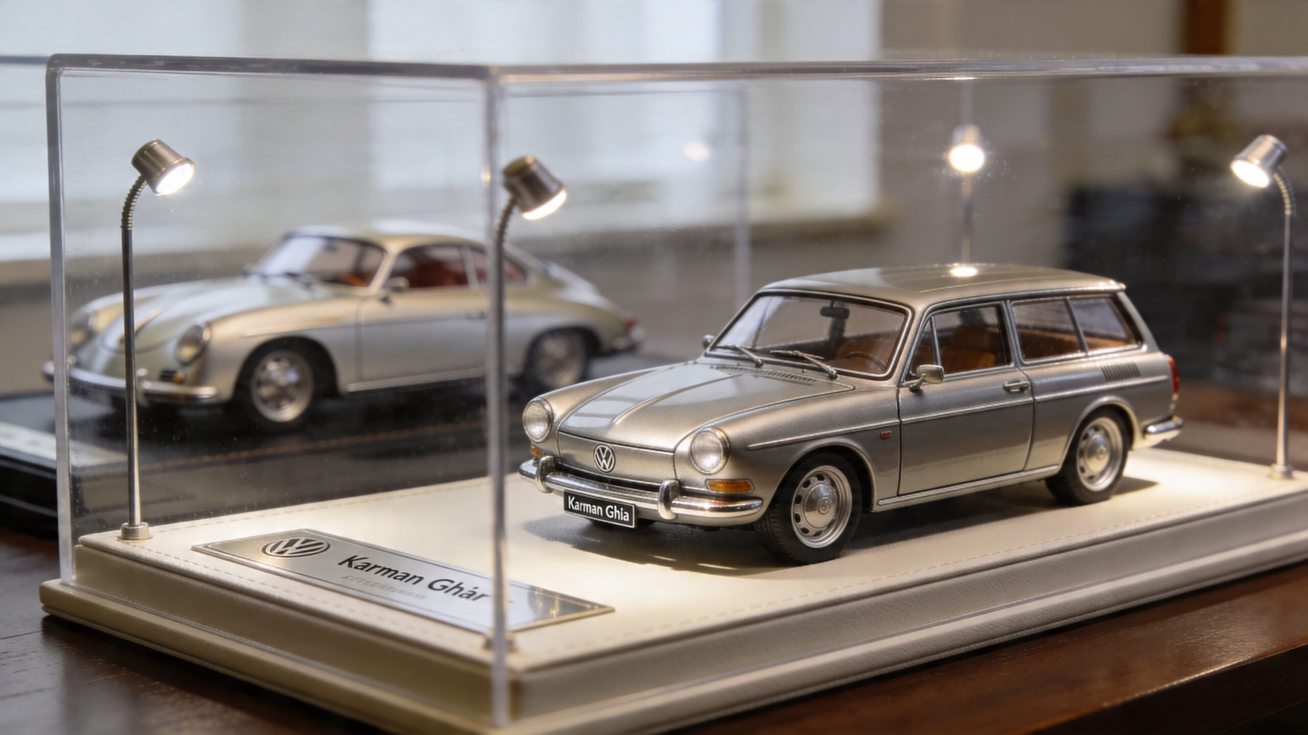 A silver Volkswagen model car displayed in a glass case with interior lighting alongside another car.