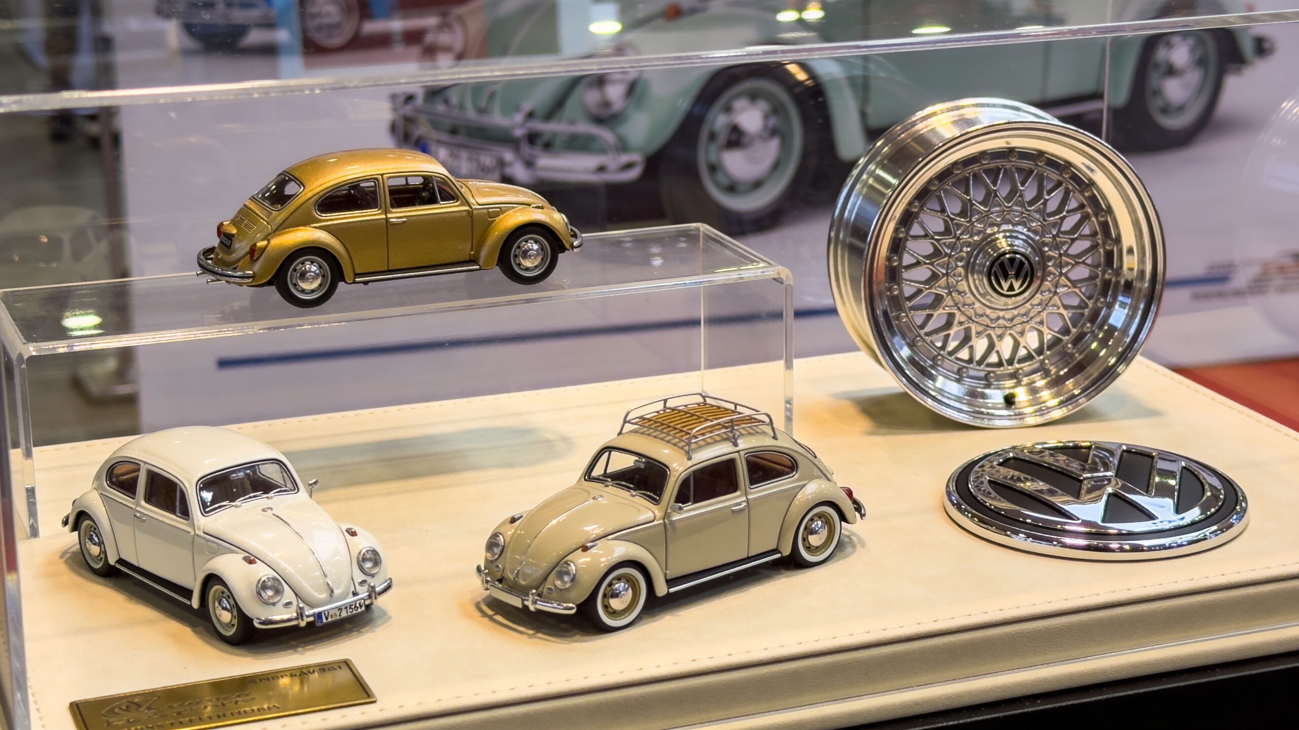 A display case featuring three miniature Volkswagen Beetle models, a metallic alloy wheel, and a VW emblem.