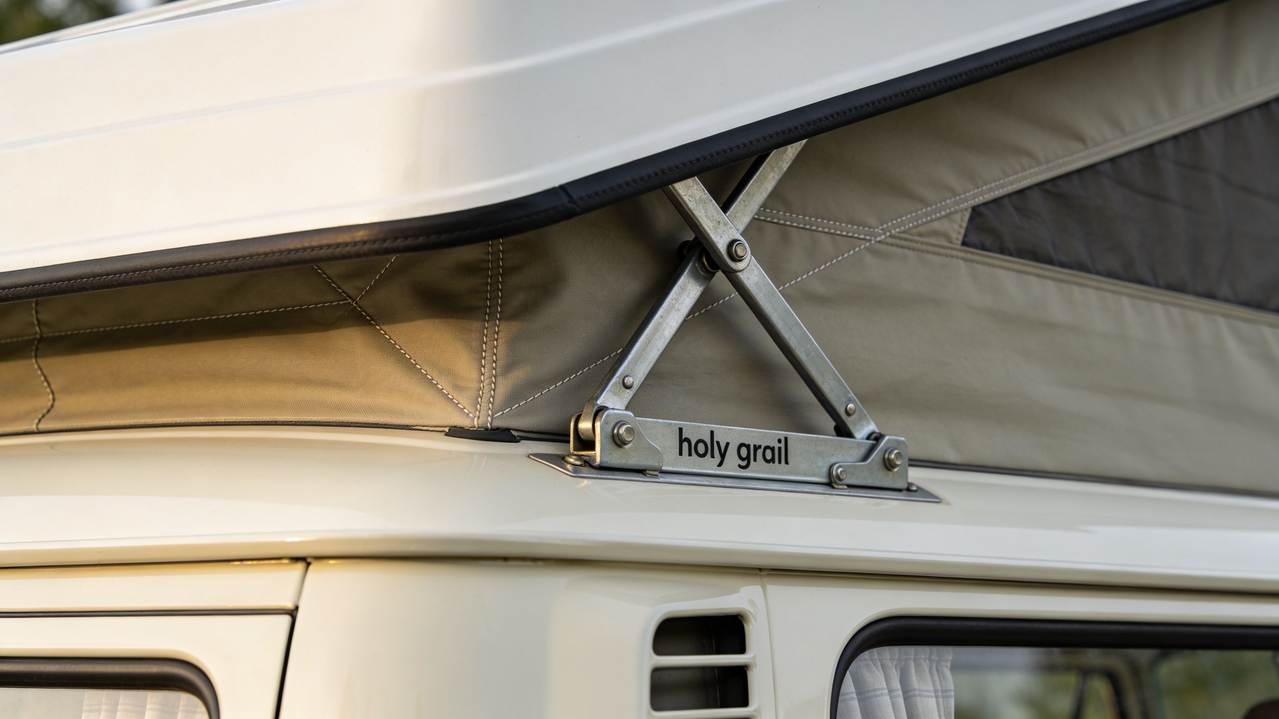 A close-up view of a metal scissor hinge mechanism supporting the pop-top roof on a camper van.
