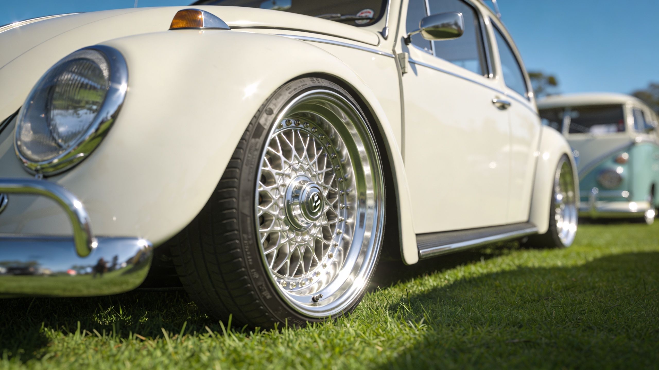 A close-up view of a custom chrome rim on a vintage white Volkswagen Beetle car.