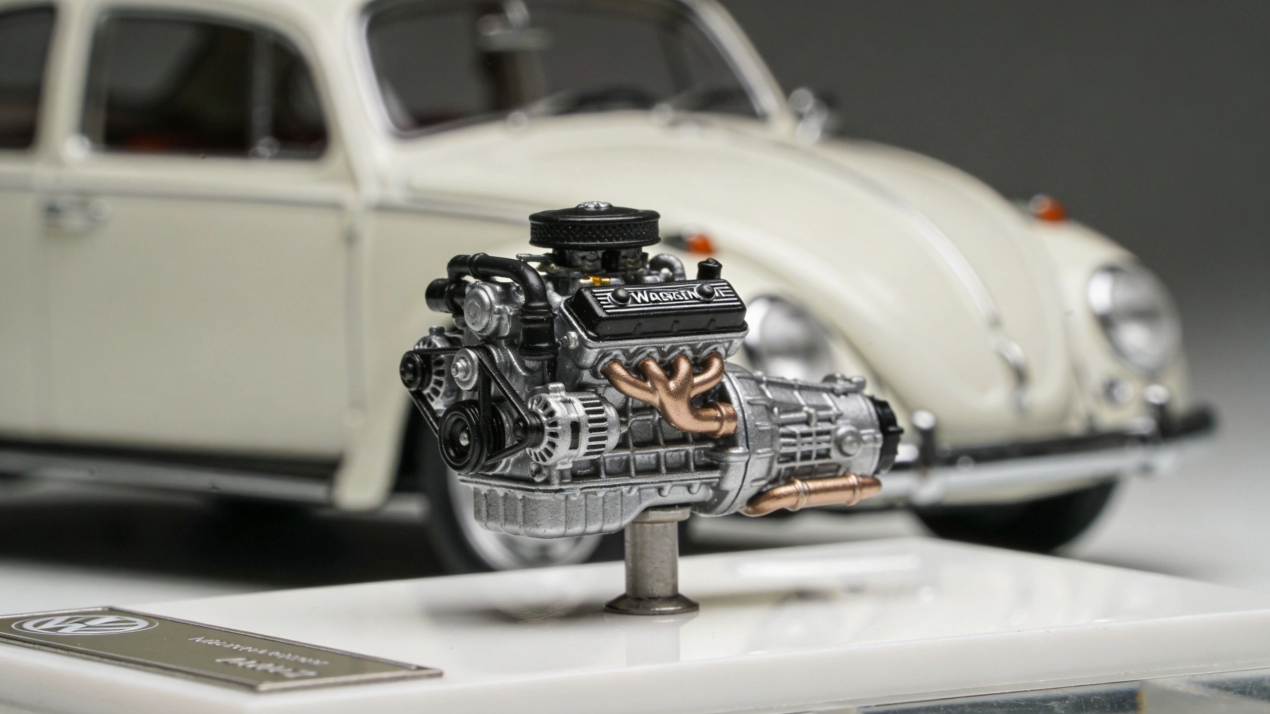 A detailed model of a Volkswagen Beetle engine displayed on a stand in front of the car.