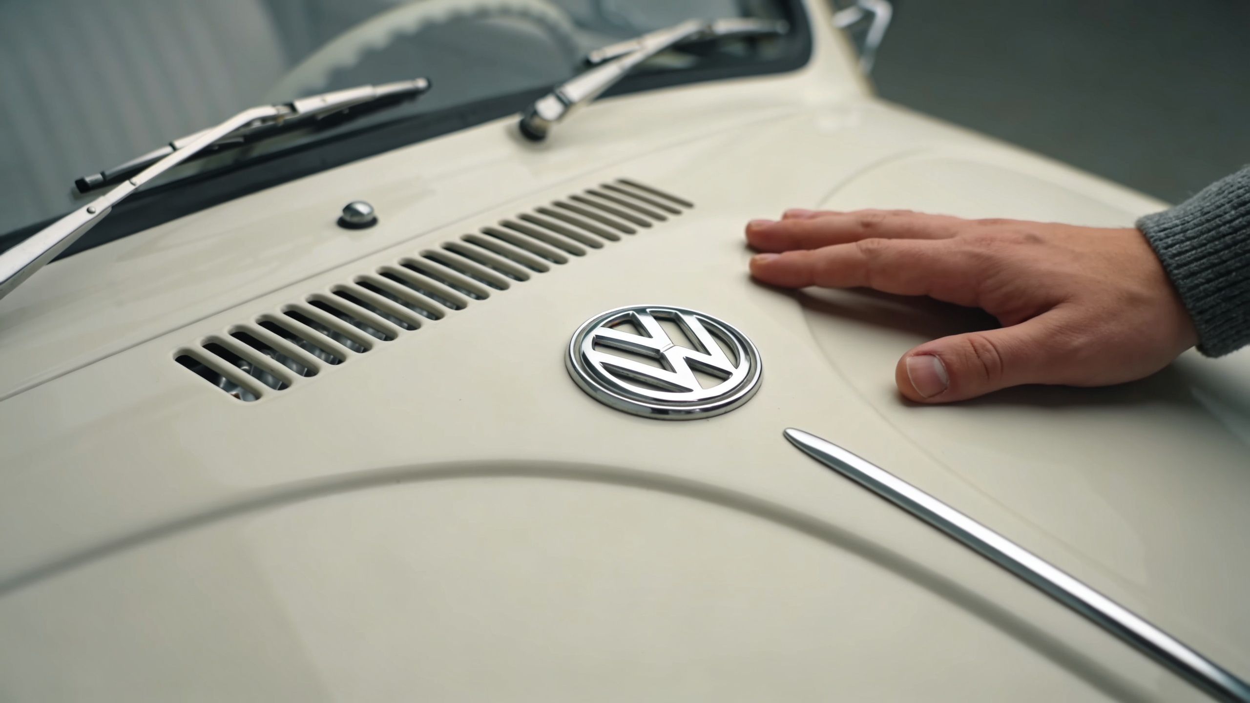 A close-up view of a hand touching the hood of a vintage white Volkswagen Beetle car.