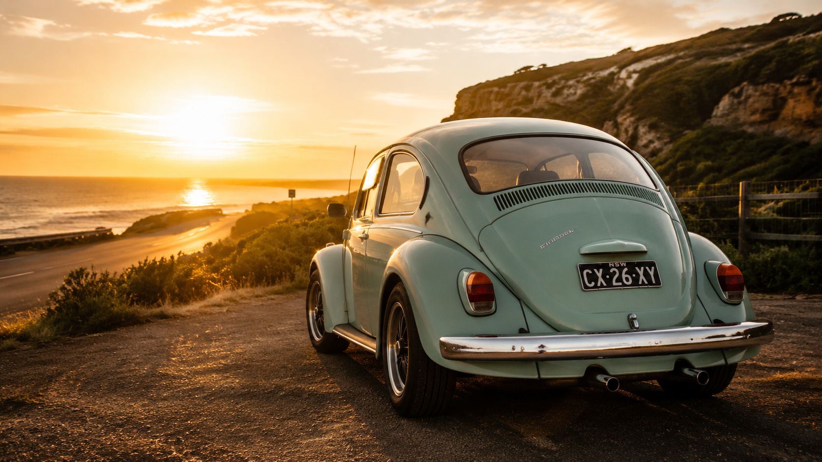 A vintage light blue Volkswagen Beetle parked on a coastal road during a beautiful golden sunset.