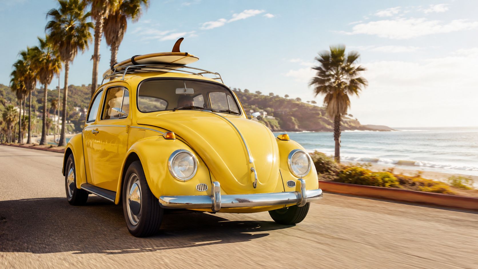 A vibrant yellow vintage Volkswagen Beetle driving along a coastal road with a surfboard on the roof.