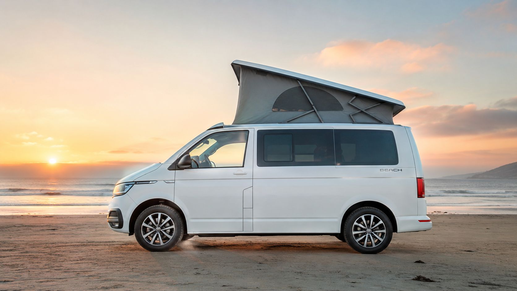 A white Volkswagen California Beach camper van parked on a sandy beach during a beautiful sunset.