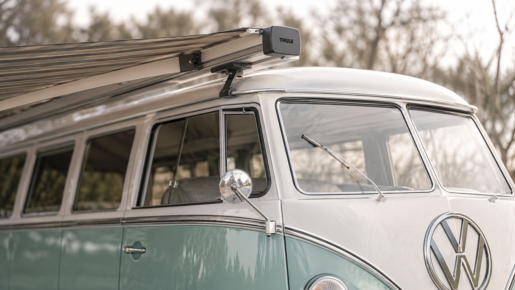 A close-up view of a vintage white and light blue Volkswagen camper van with a Thule awning.