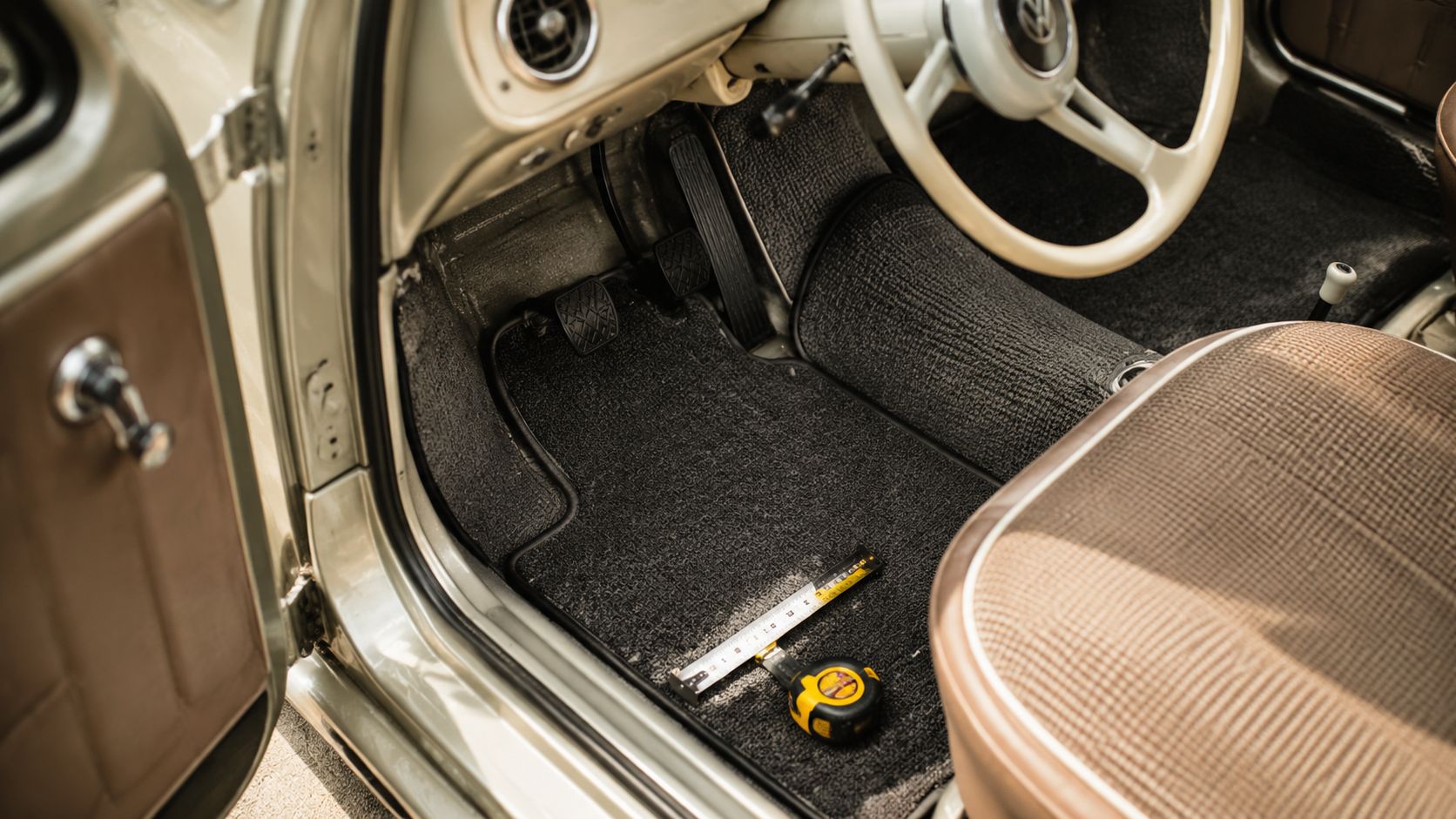 A tape measure lying on a black custom floor mat inside a vintage Volkswagen beetle interior.