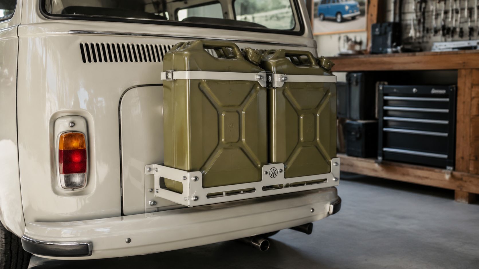 A beige Volkswagen bus featuring a white metal rack holding two olive green jerry cans on the back.