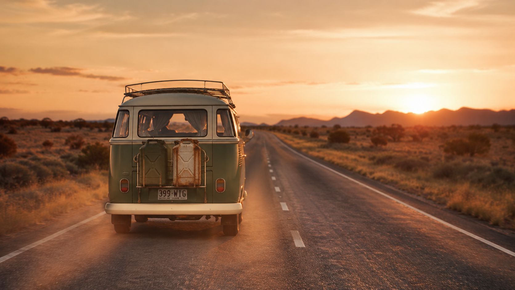 A vintage Volkswagen camper van driving down a desert highway during a beautiful orange sunset.