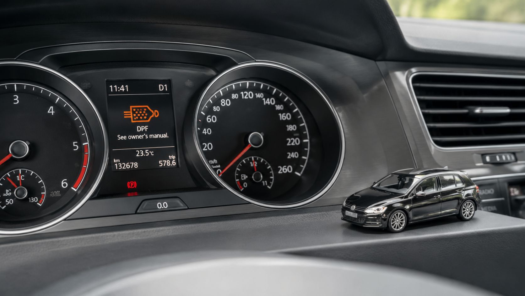 A car dashboard displaying a DPF filter warning light alongside a miniature black Volkswagen car model.