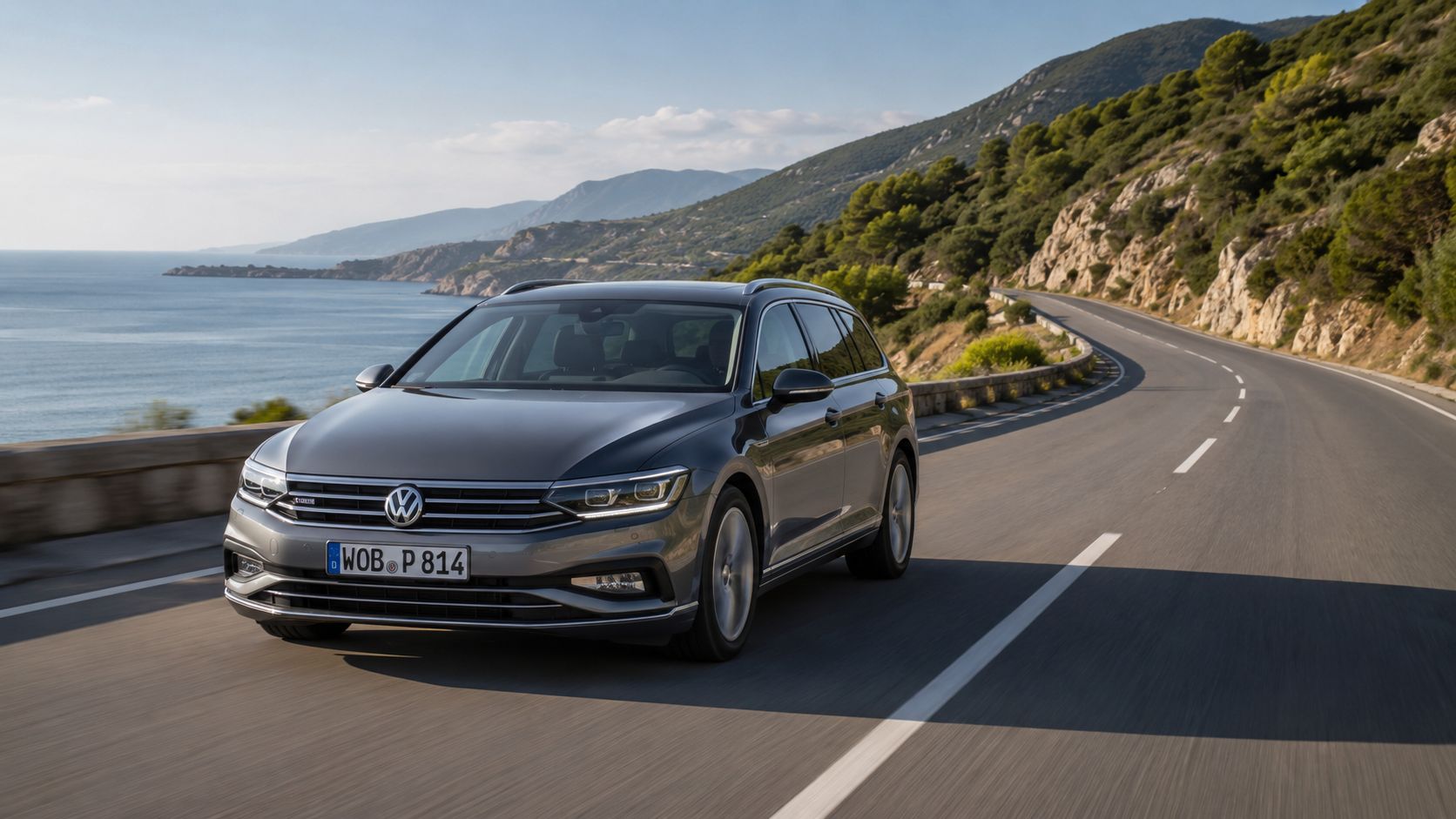 A silver Volkswagen Passat station wagon driving along a scenic coastal road during a sunny day.