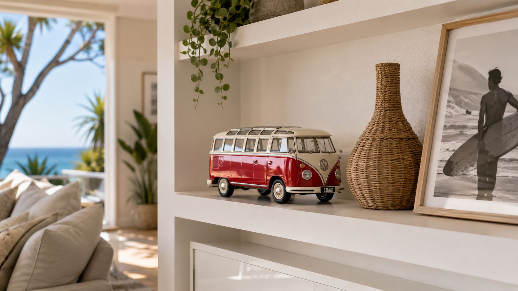 A miniature red and white Volkswagen van sits on a white shelf next to a wicker vase.