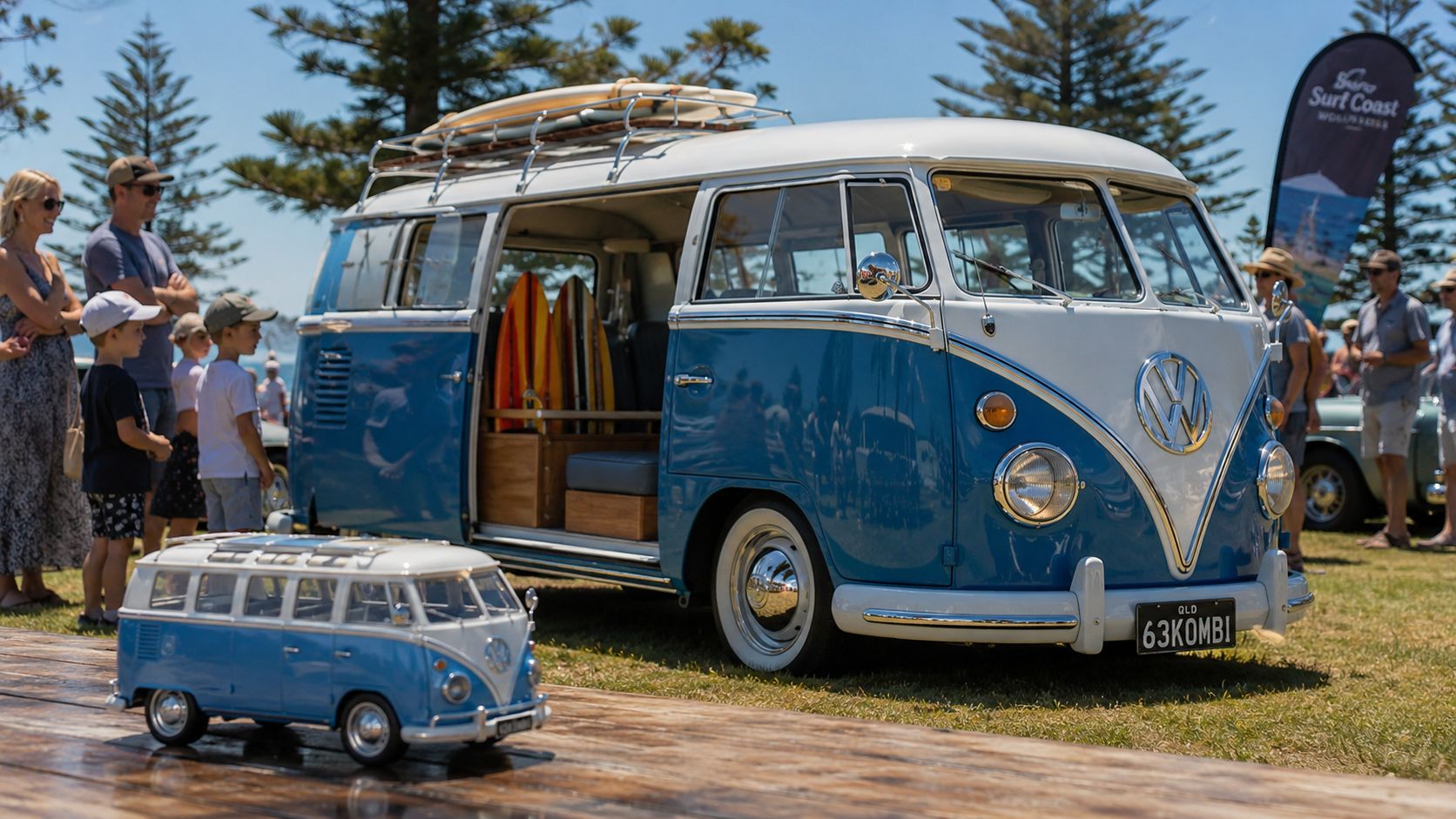 A classic blue and white Volkswagen Type 2 bus parked on grass next to a miniature model.