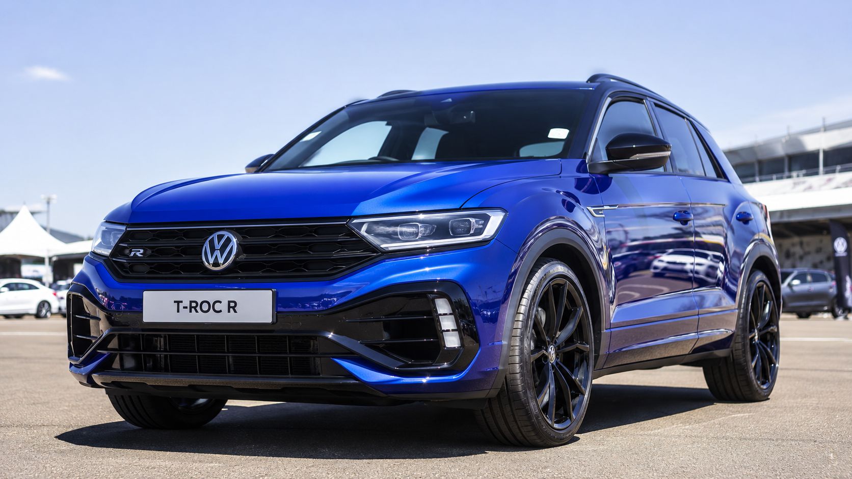 A sleek blue Volkswagen T-Roc R compact SUV parked outdoors on a sunny day at a track.