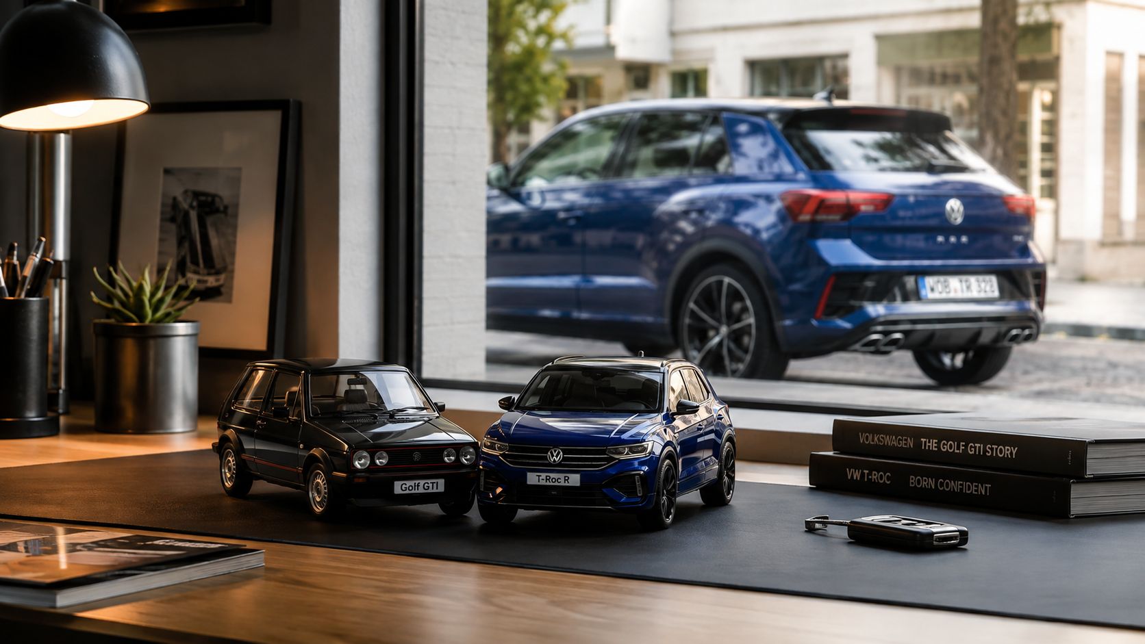 A miniature Golf GTI and a T-Roc R model car sit on a desk with books.