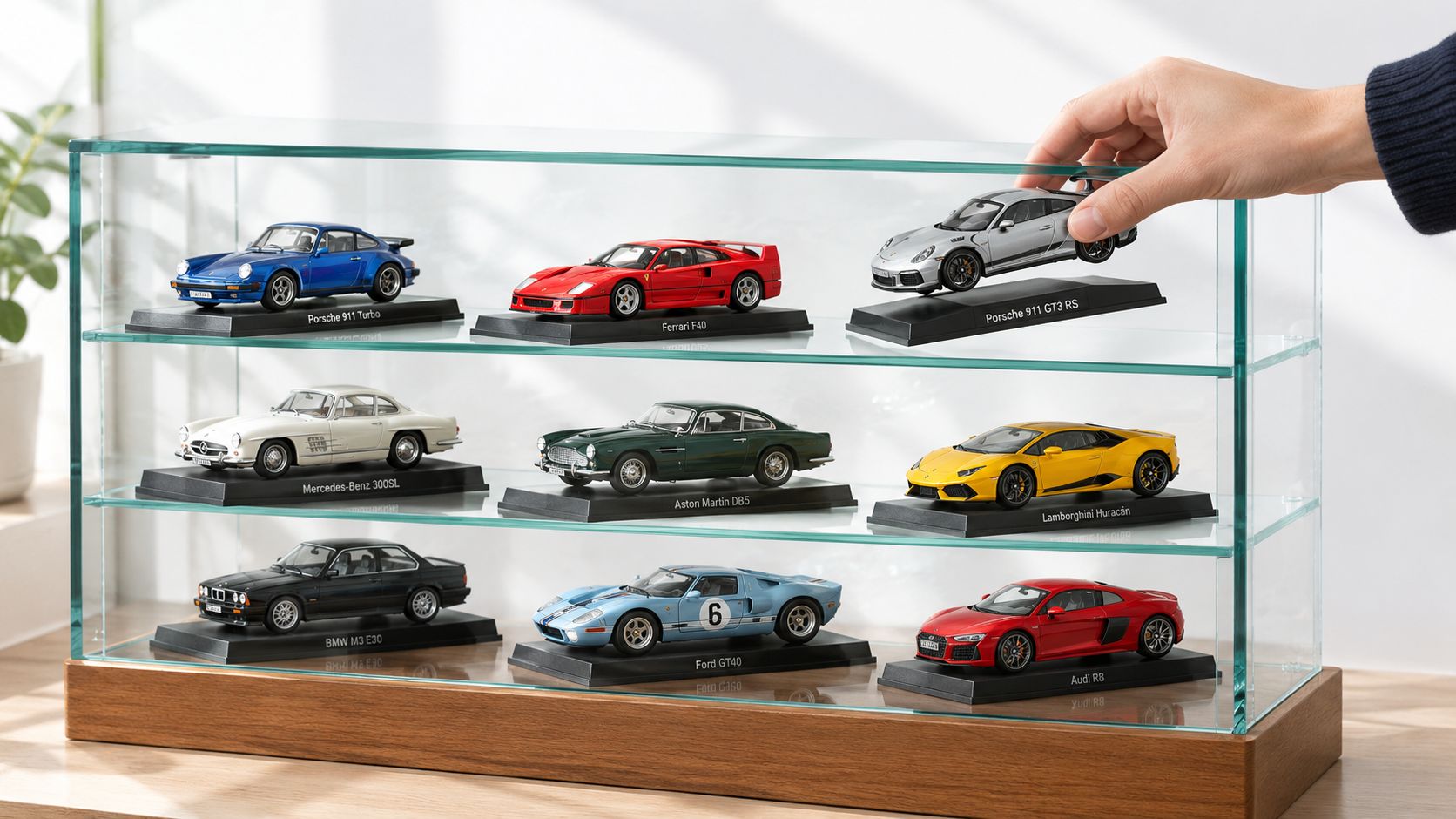 A hand placing a silver Porsche 911 GT3 RS diecast model into a three-tiered glass display case.