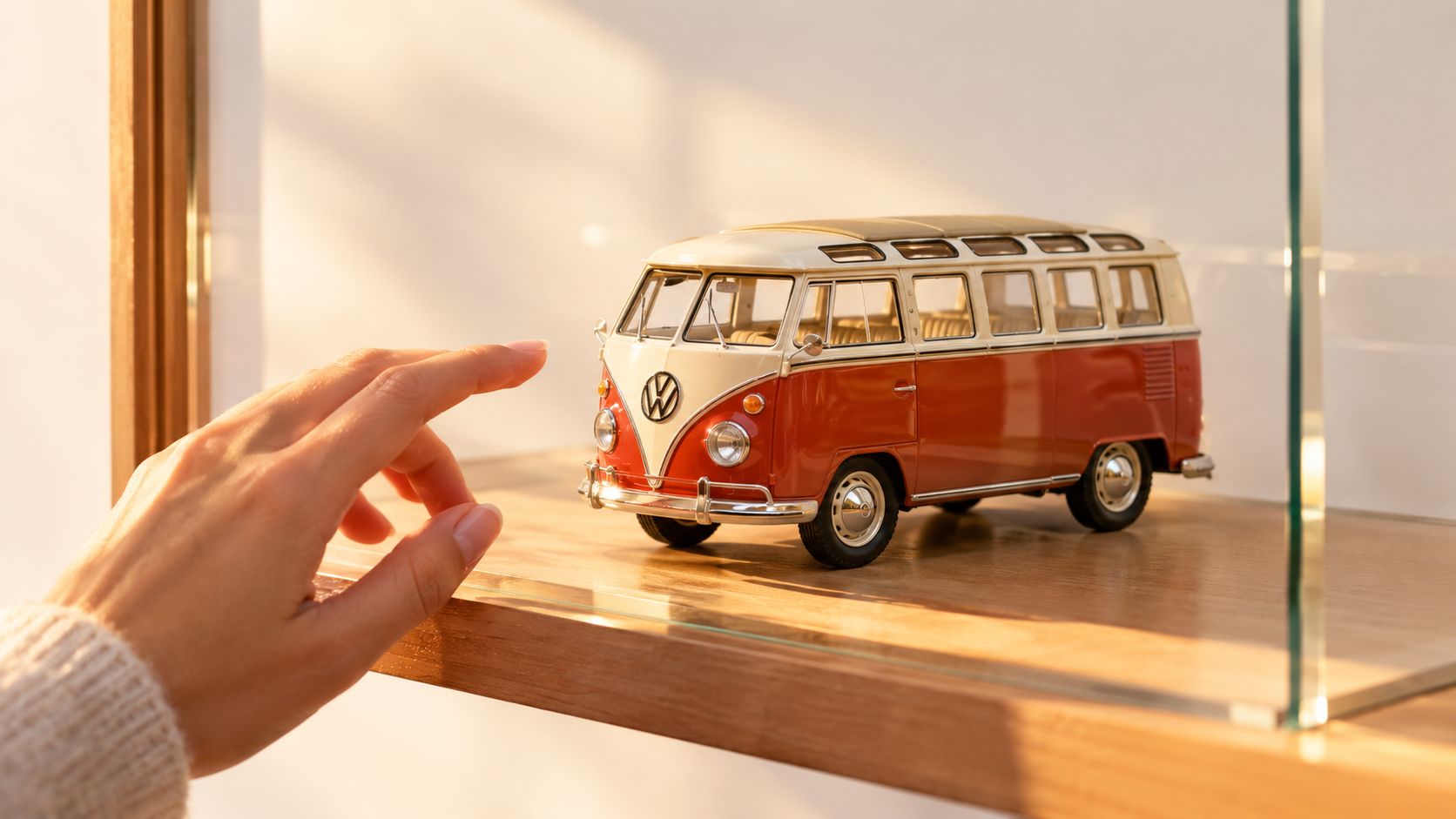 A close-up view of a hand reaching toward a miniature red and white Volkswagen bus model.