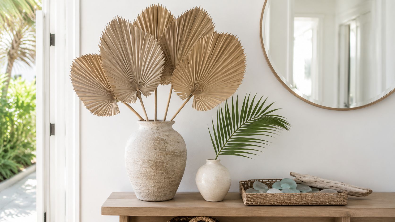 A rustic entryway table features dried palm leaves in a vase and a green palm frond nearby.