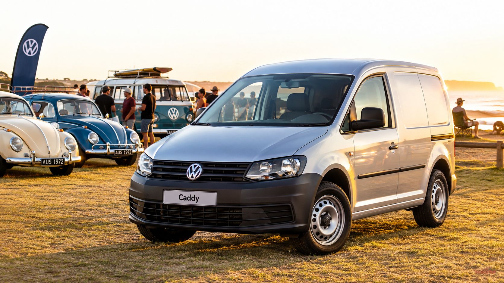 A silver Volkswagen Caddy van parked on a grassy field at sunset near other classic Volkswagen vehicles.