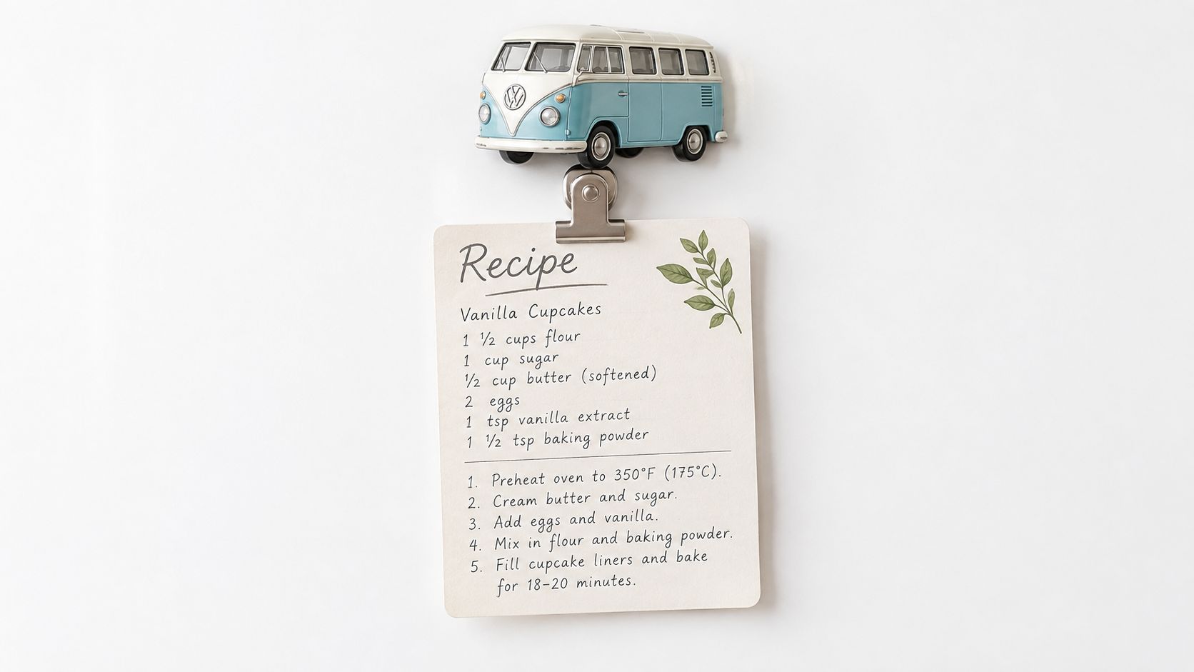 A small recipe card for vanilla cupcakes is clipped to a white refrigerator with a toy bus magnet.