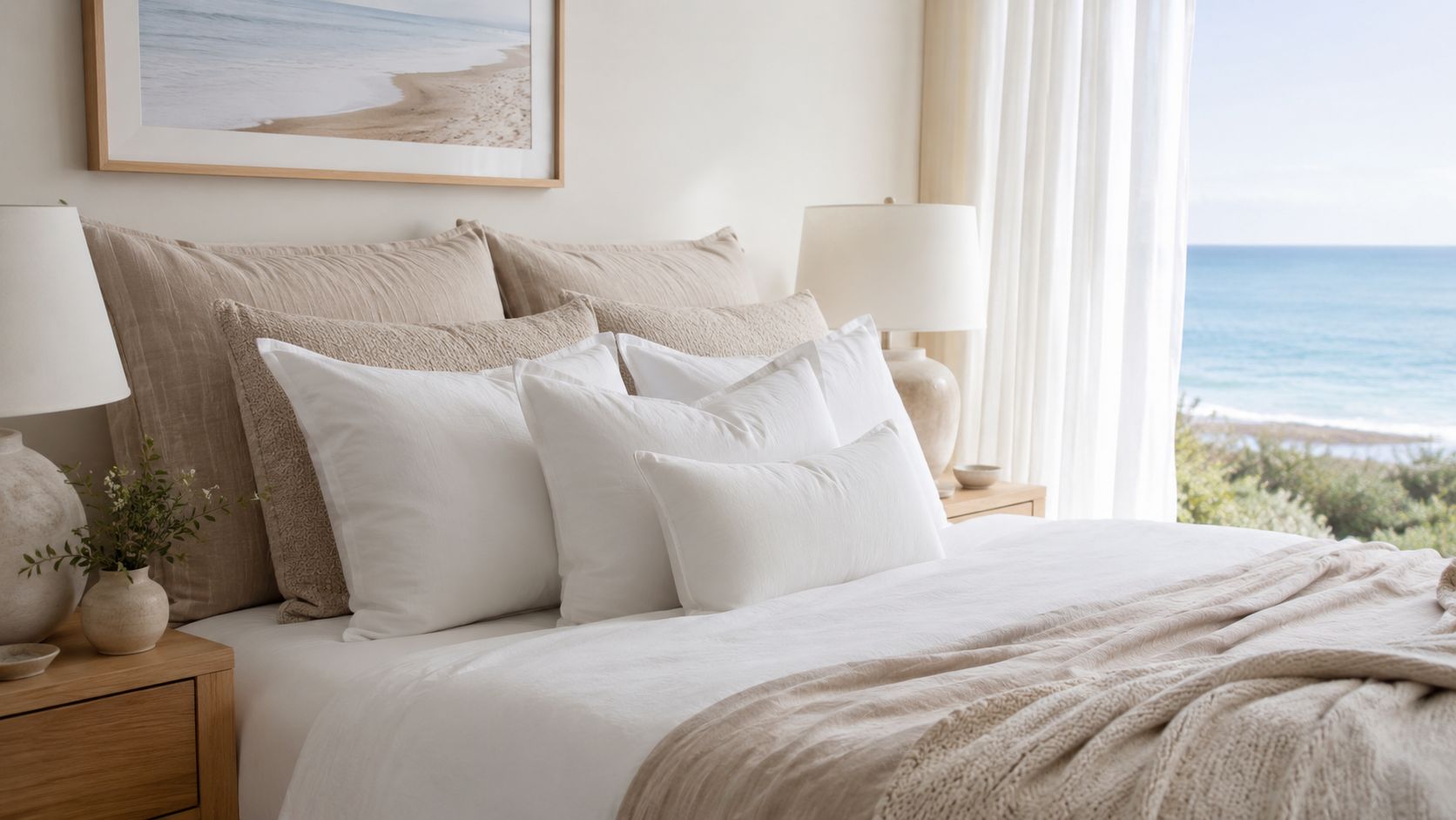 A luxurious bedroom featuring white toss pillows on a beige bed with a scenic ocean view.
